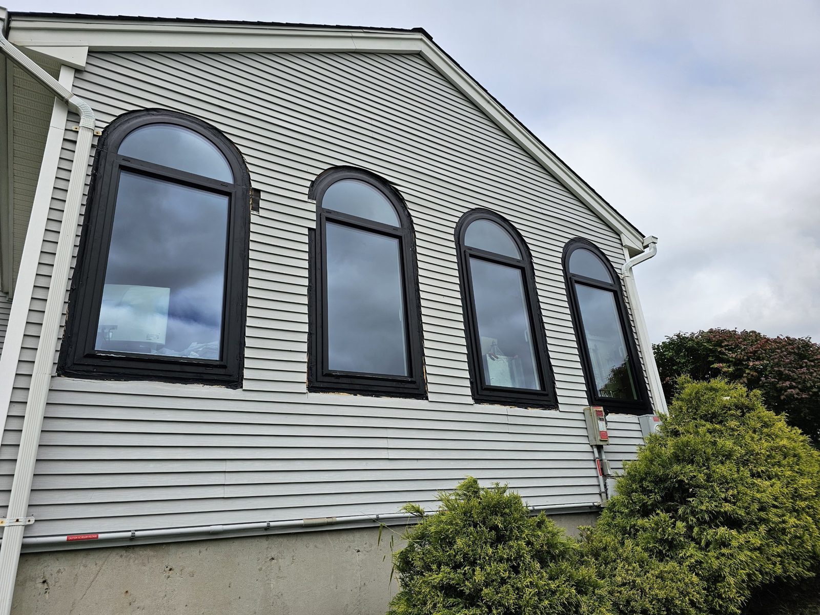 Four arched black aluminium windows on a vinyl-sided gable in Somerset NJ, seen from below