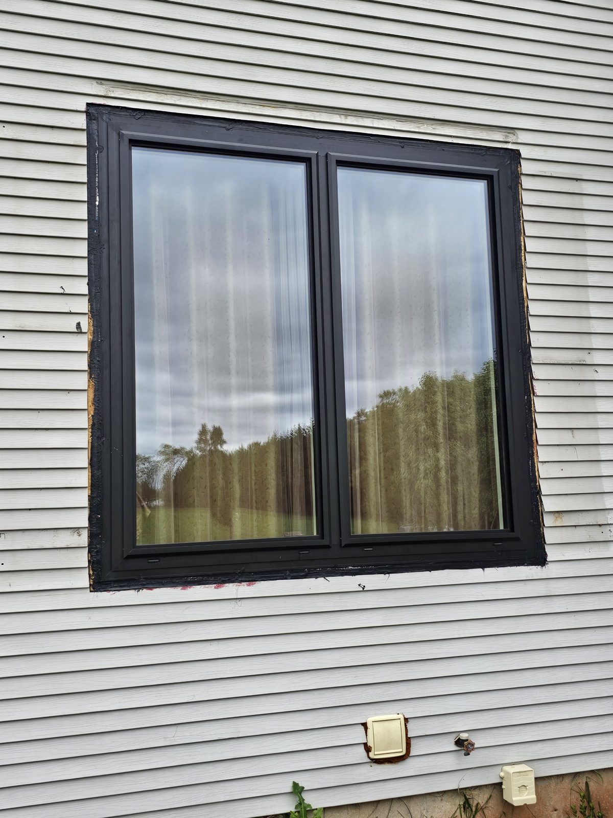 Close view of a paired black aluminium window with triple glass in white vinyl siding, Somerset NJ