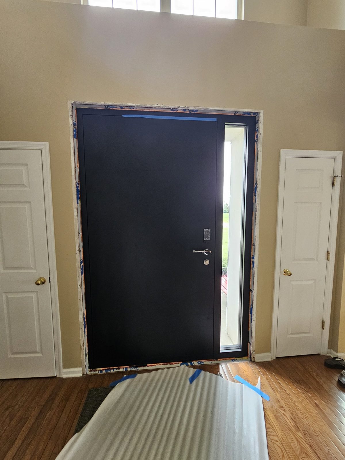 New black aluminium entry door with sidelite seen from inside the two-storey entrance hall of a house in Somerset NJ