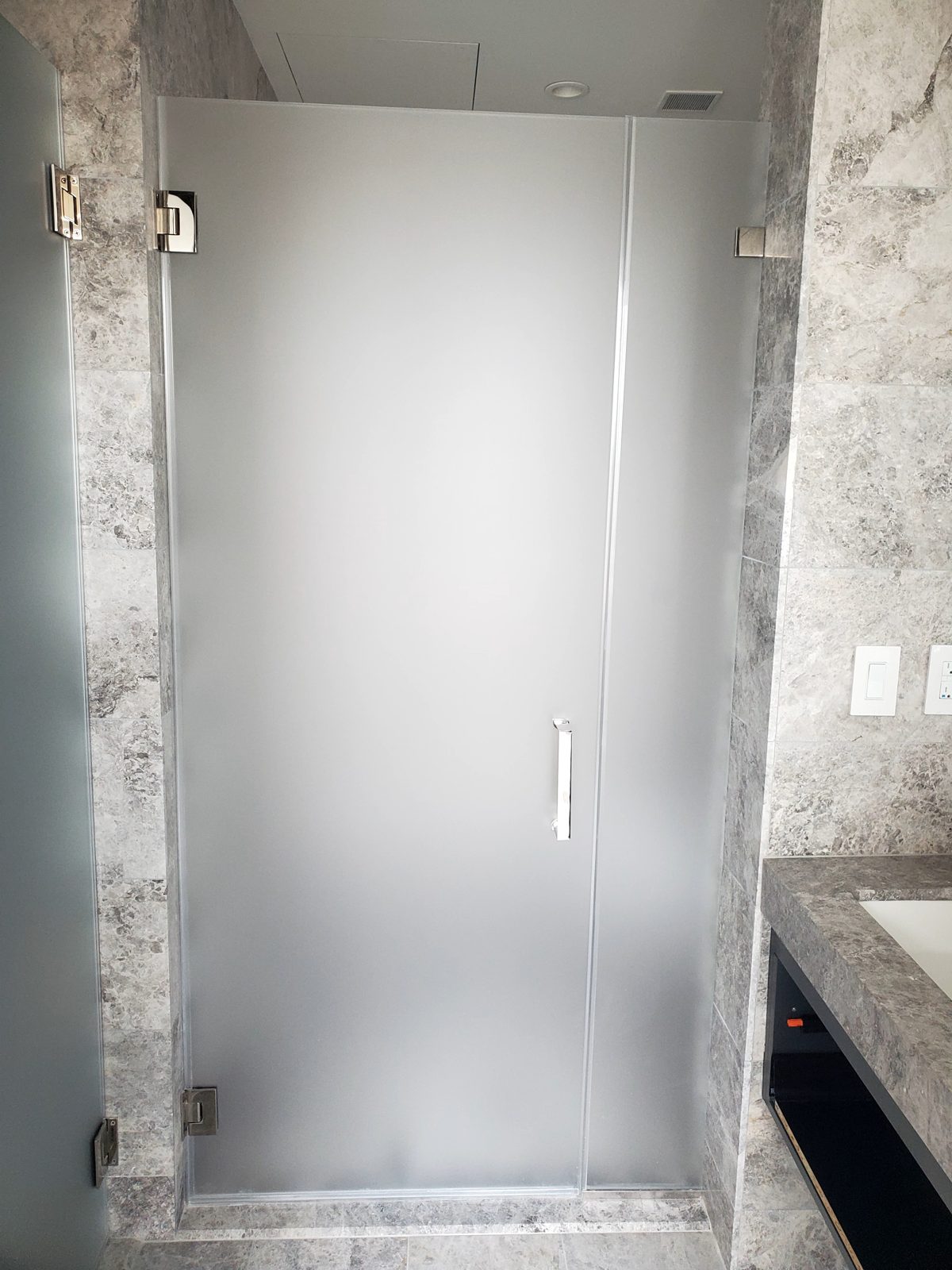 Frameless shower door and fixed side panel in velour acid-etched glass between marble walls, apartment bathroom in Tribeca, Manhattan