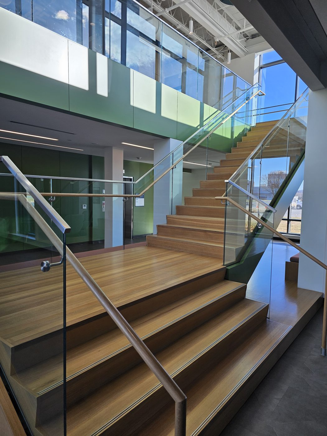Timber staircase with Q-railing frameless glass guards and wood handrails rising to the mezzanine at UGI Utilities, Bethlehem, PA