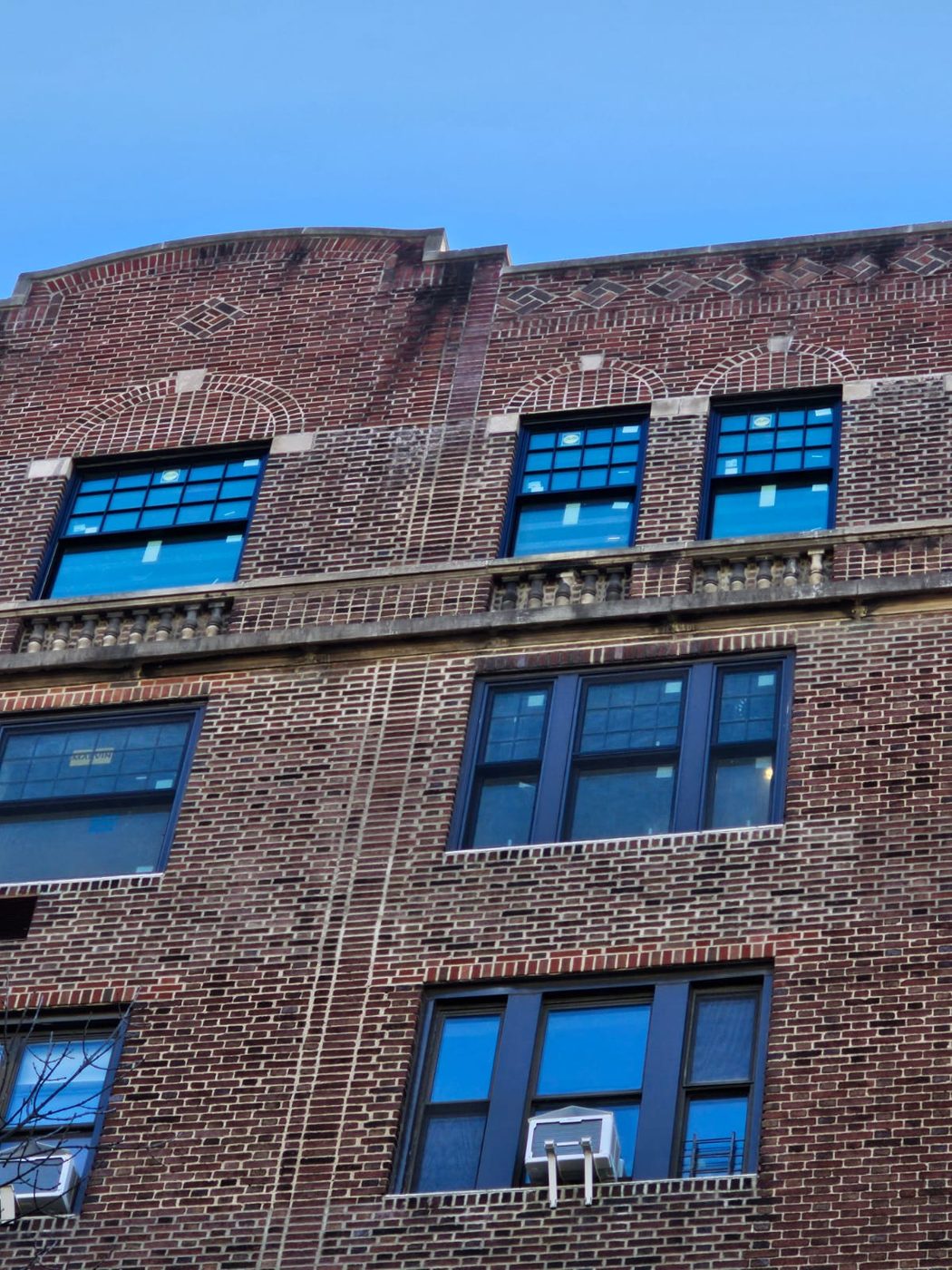 The completed elevation - dark clad sashes set into the original brick openings, with the decorative brickwork and arched heads untouched &mdash; Upper West Side, Manhattan