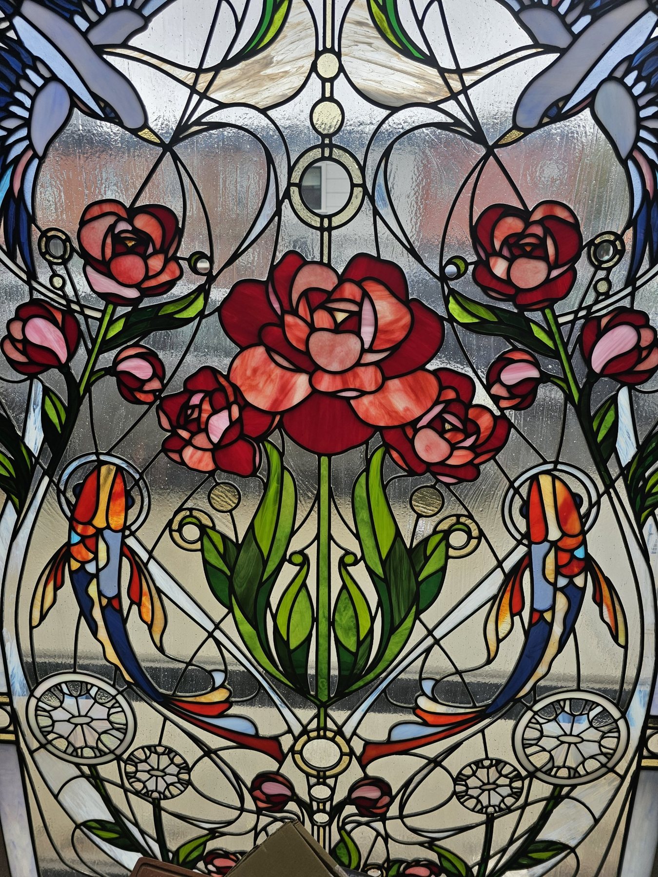 Close detail of a stained glass panel showing roses, koi fish, leaves and the raised solder lines between pieces of textured art glass